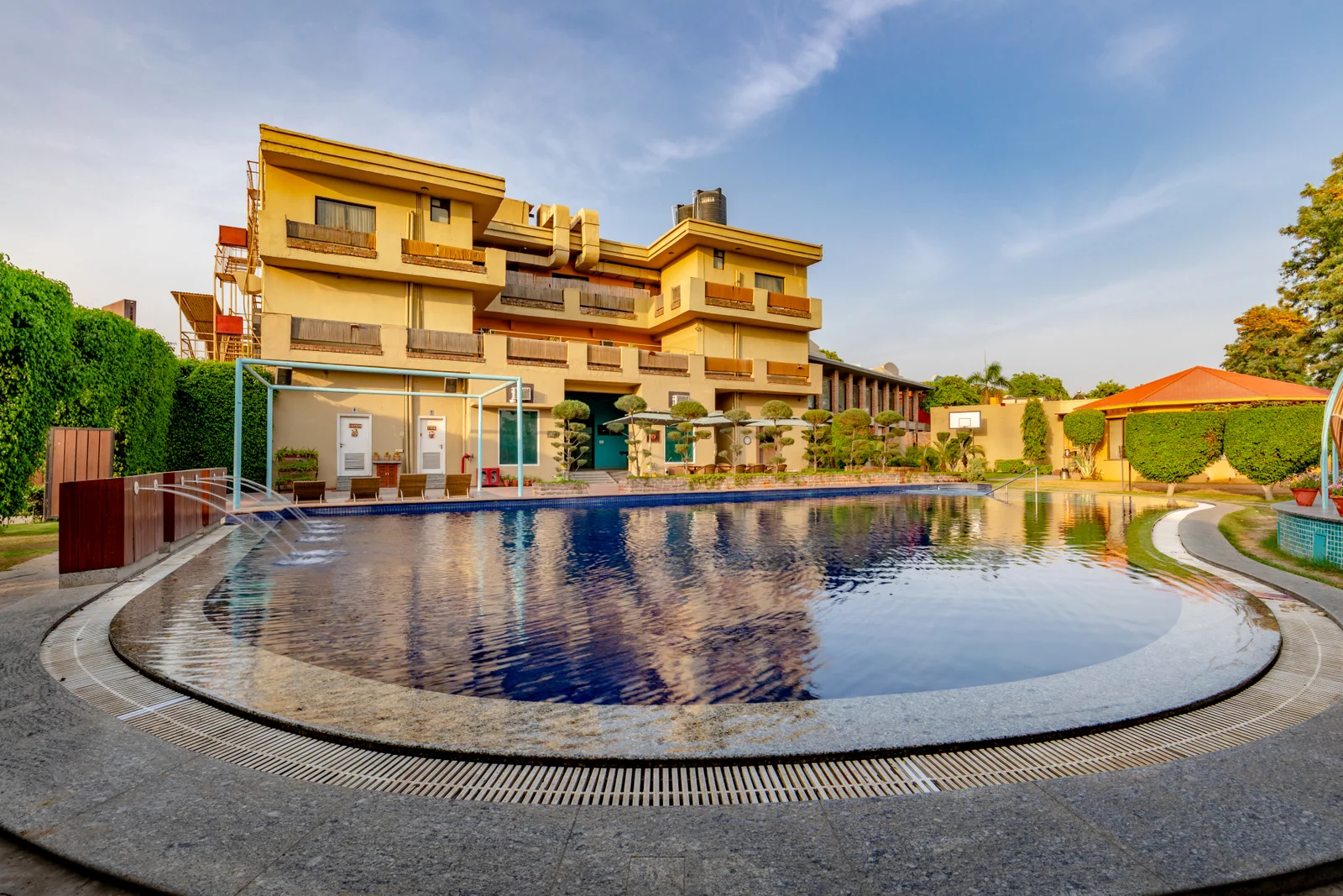 Large outdoor swimming pool and multi-storey resort building facade at Aravali Resort