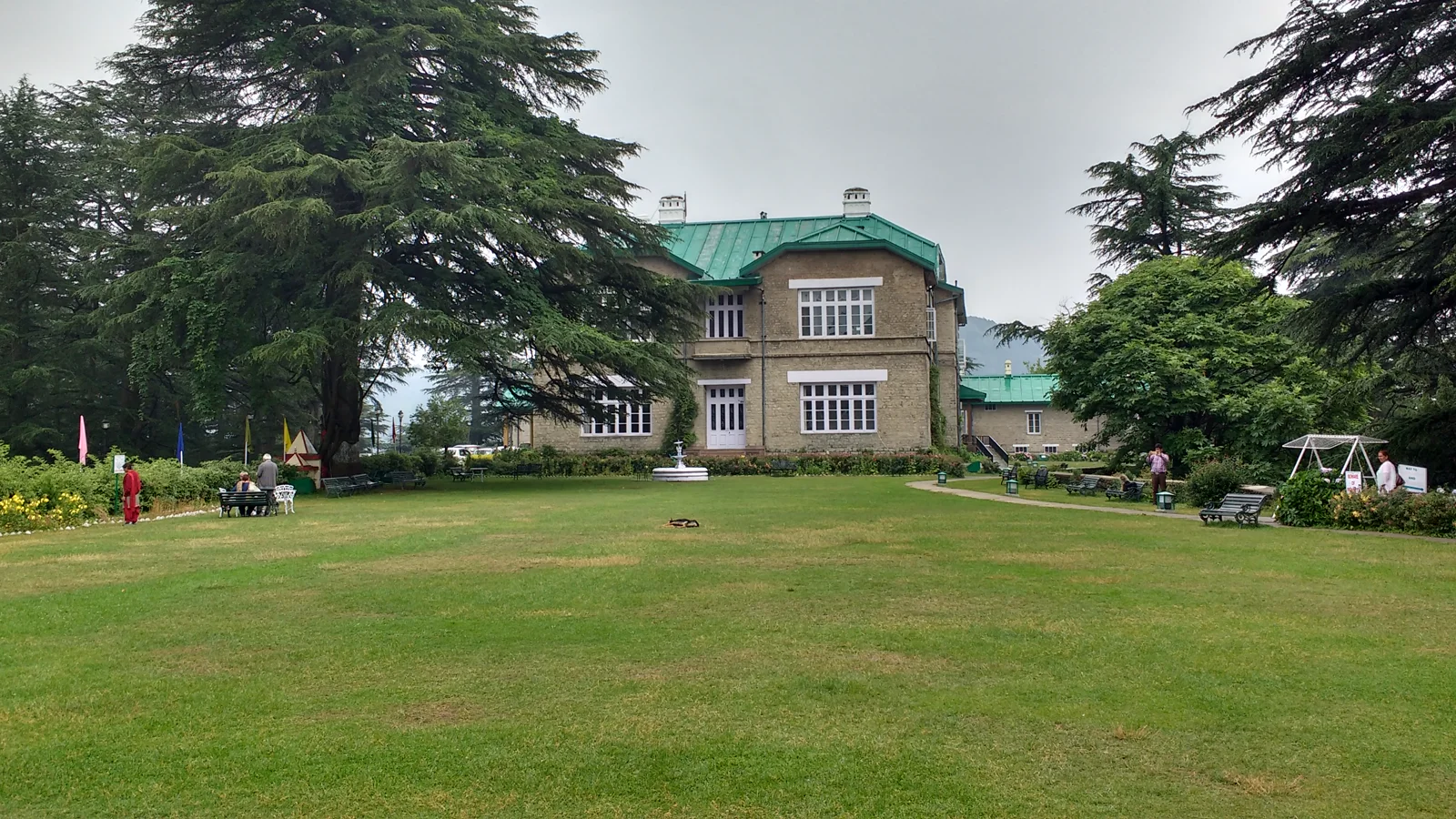 Manicured green resort lawn with garden seating surrounded by tall Himalayan deodars