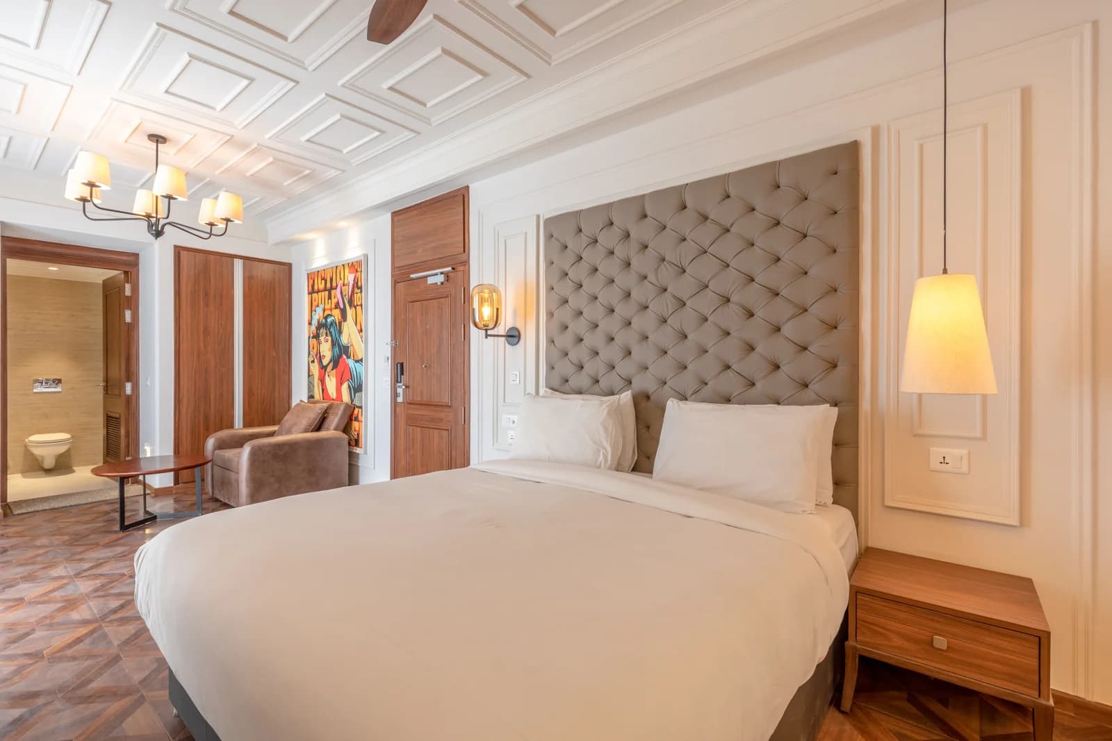 Side angle view of deluxe king suite bed with bedside pendant lighting and vanity mirror