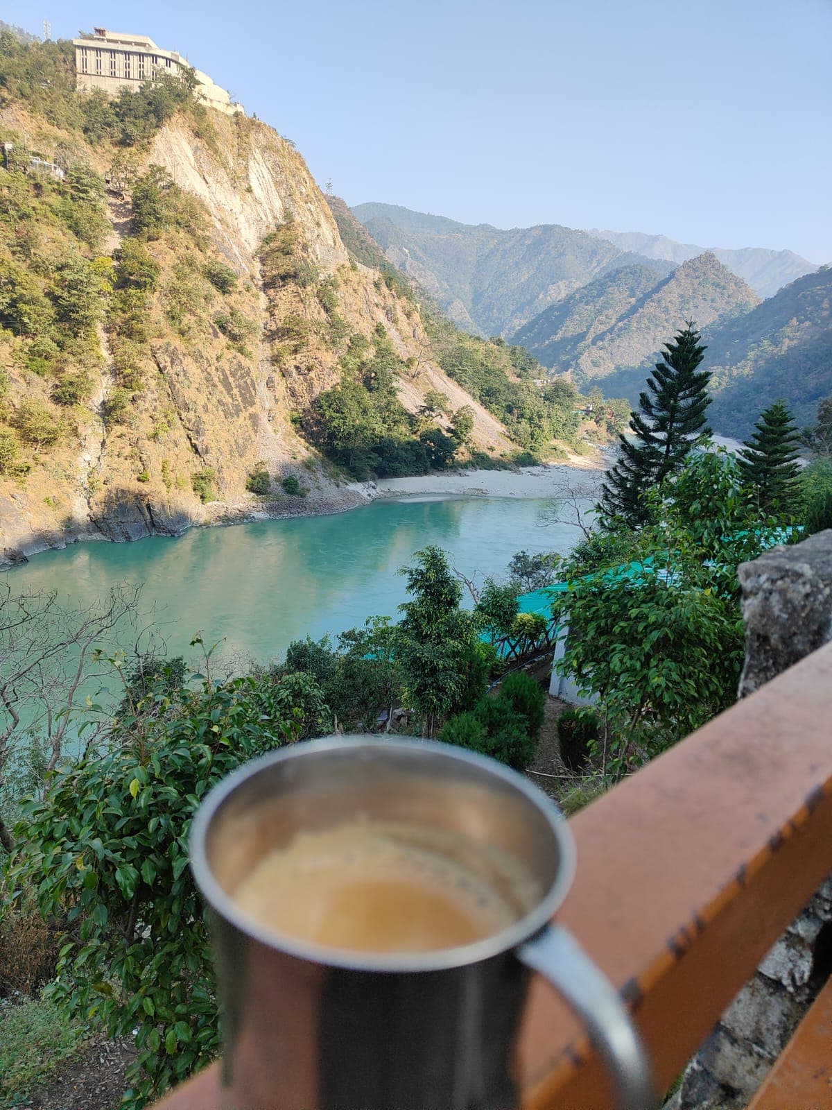 Steel mug of morning tea on the balcony railing overlooking the turquoise Ganga river