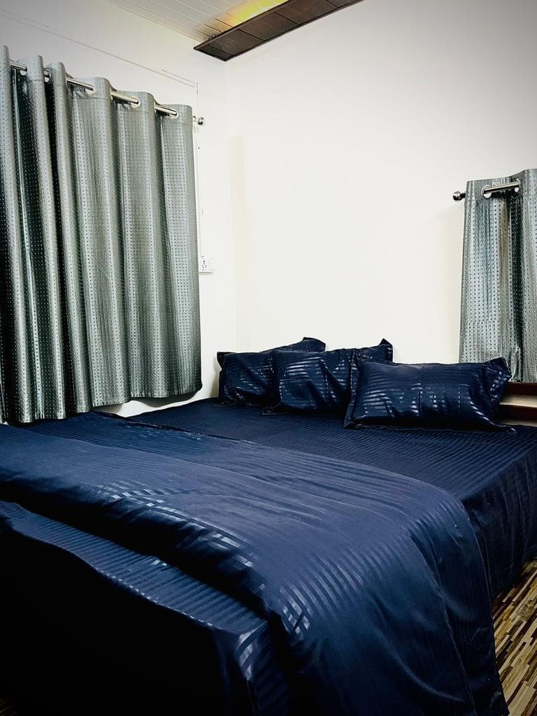 Side angle of made bed with dark blue linens inside Byasi cottage room
