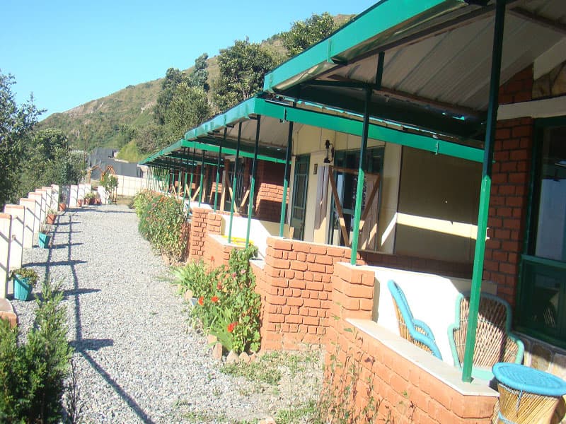 Cottage verandas with cane chairs and gravel pathway at Chakrata Camps & Cottages