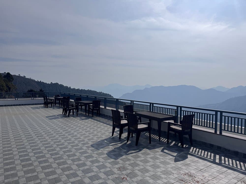 Open rooftop terrace viewing deck overlooking pine forest slopes in Kanatal