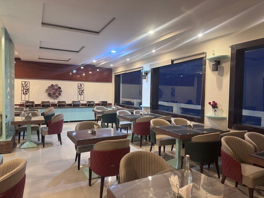Indoor restaurant dining room with panoramic glass windows overlooking Kanatal hills