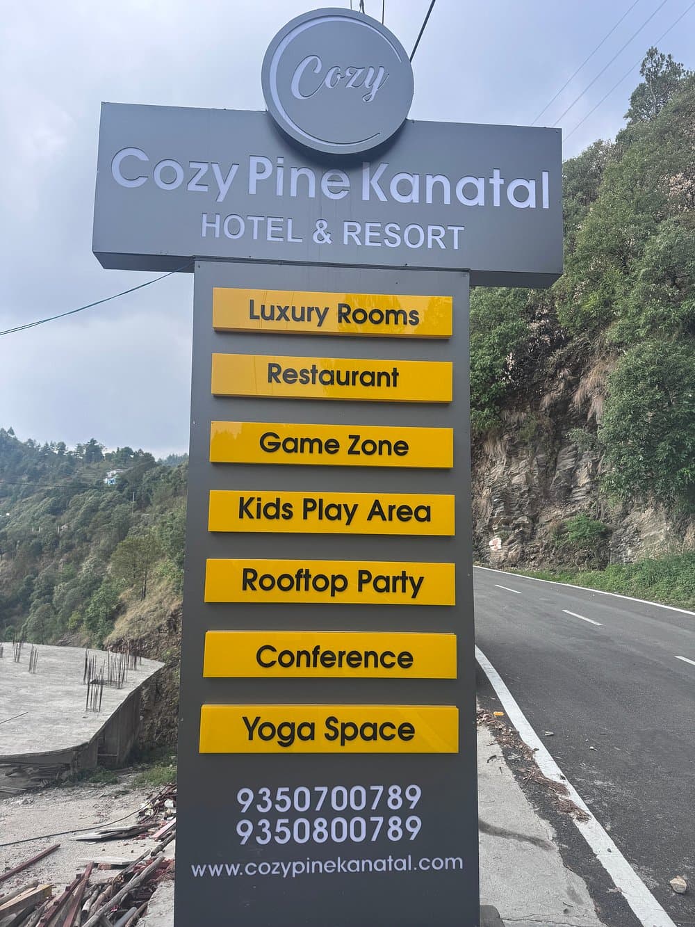 Roadside brand signboard for Cozy Pine Kanatal Hotel and Resort listing amenities